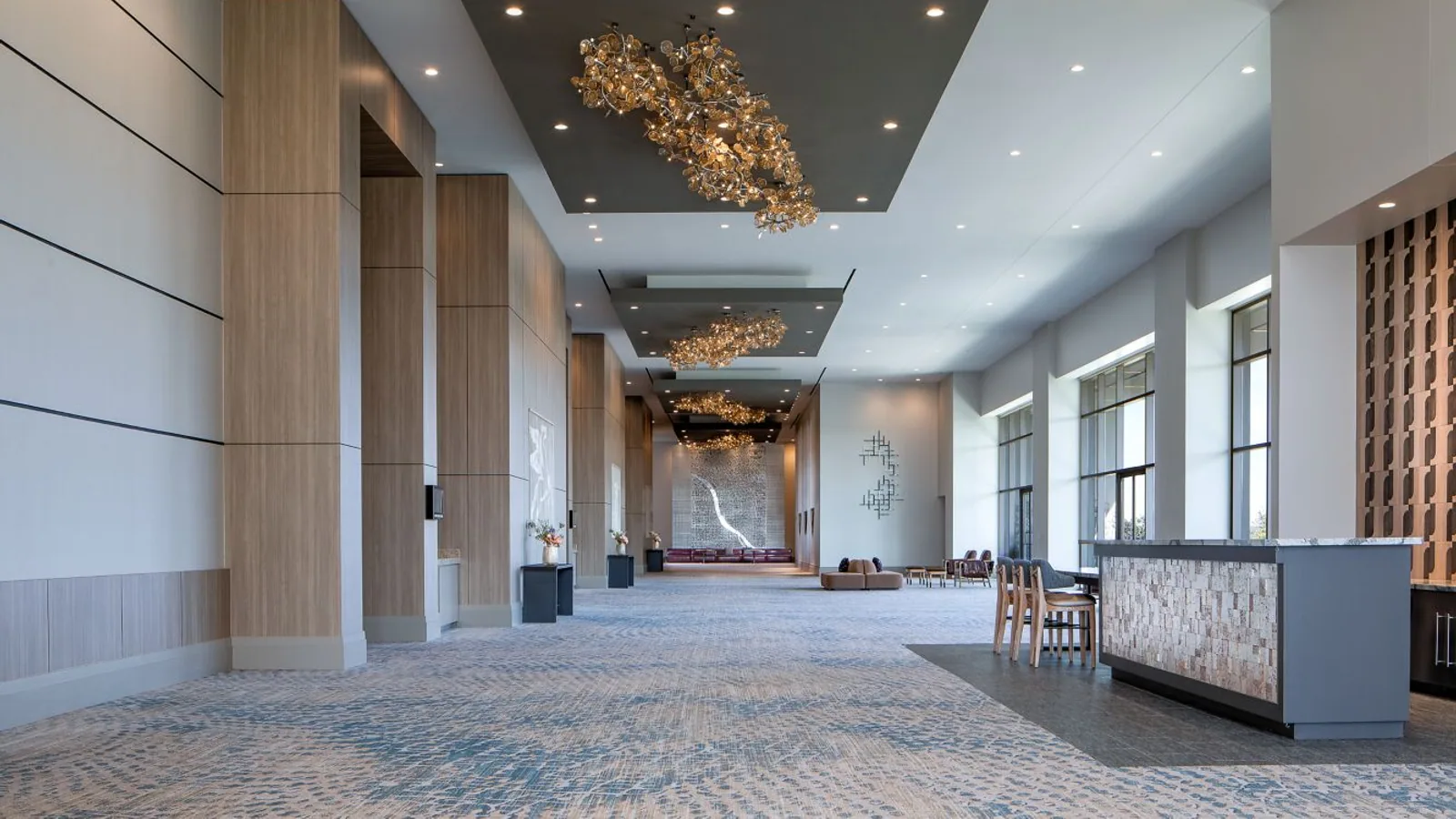 Long hotel ballroom foyer with finished walls, wood panels, and coordinated ceiling details.