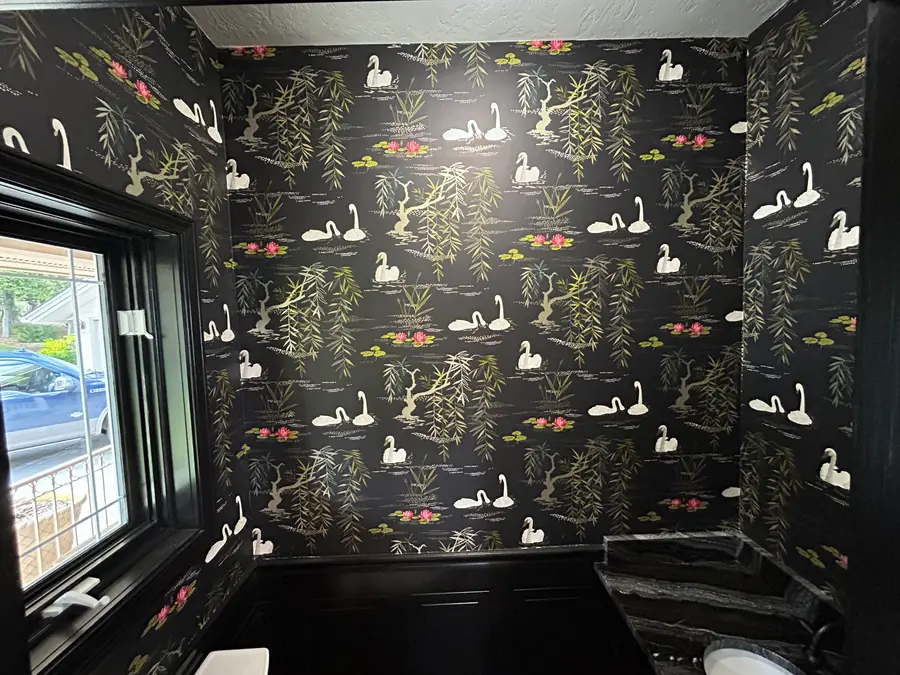 Powder room wrapped in black wallpaper with white swans, willow branches, and pink water lilies.
