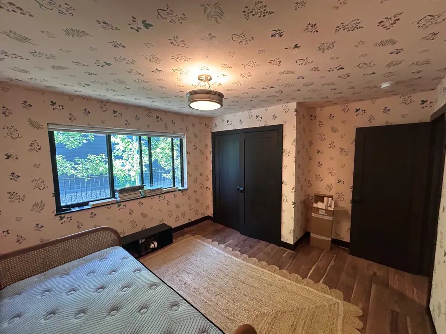 Delicate botanical wallpaper installed across the walls and ceiling of a bedroom with dark trim.