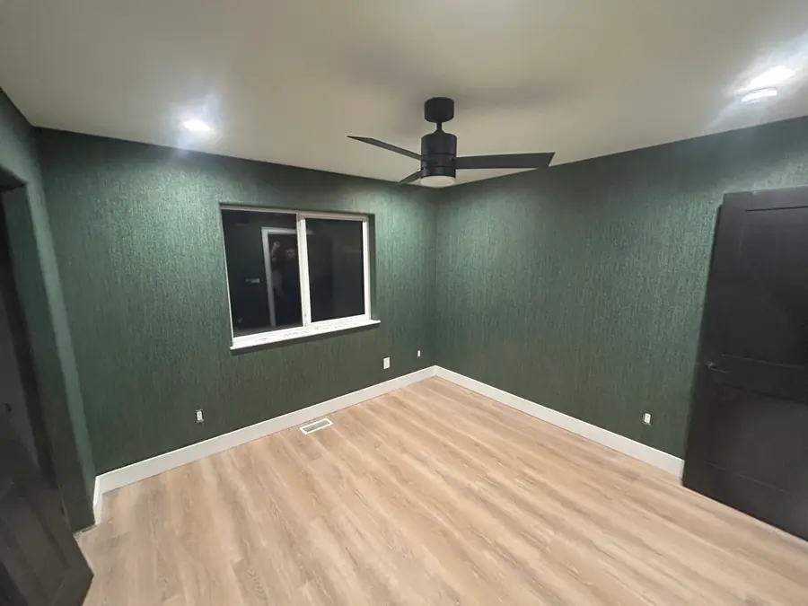 Finished room wrapped in deep green textured wallcovering with dark doors and light wood flooring.