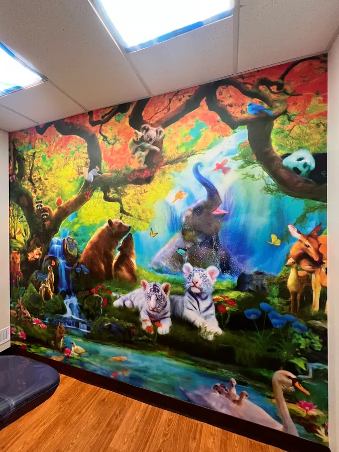 Colorful floor-to-ceiling mural wallcovering depicting animals in a forest and waterfall scene.