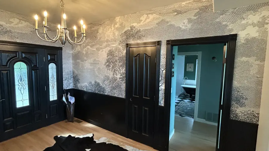 Monochrome landscape mural wallcovering framed by dark trim in a residential foyer.