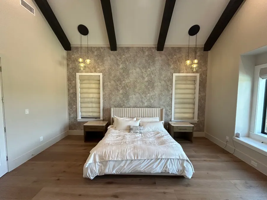 Soft taupe textured wallcovering installed on a vaulted bedroom feature wall framed by dark beams and pendant lights.