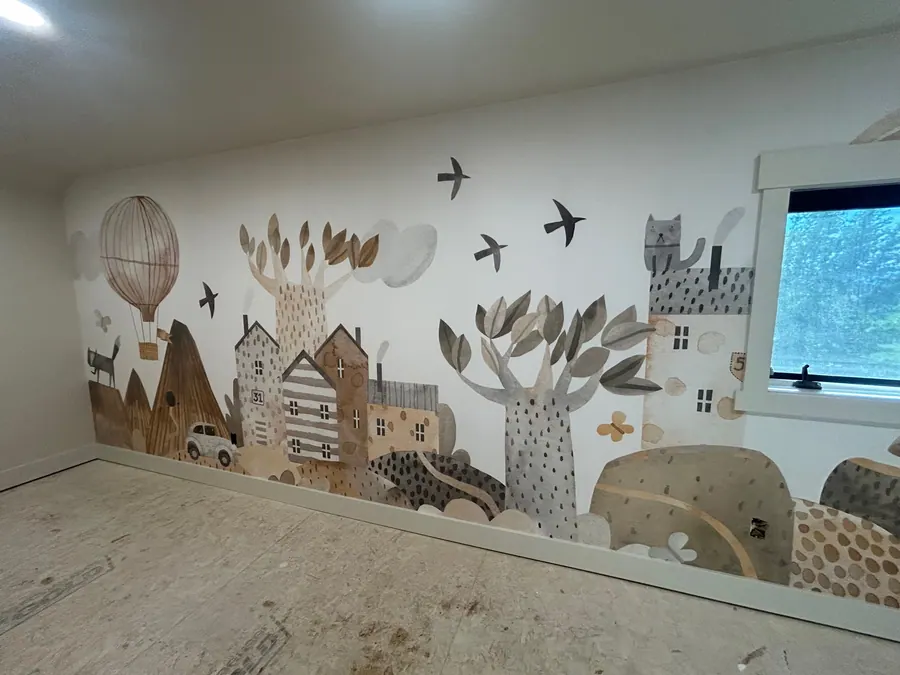 Whimsical neutral-toned town mural wallcovering installed across a children's room feature wall.